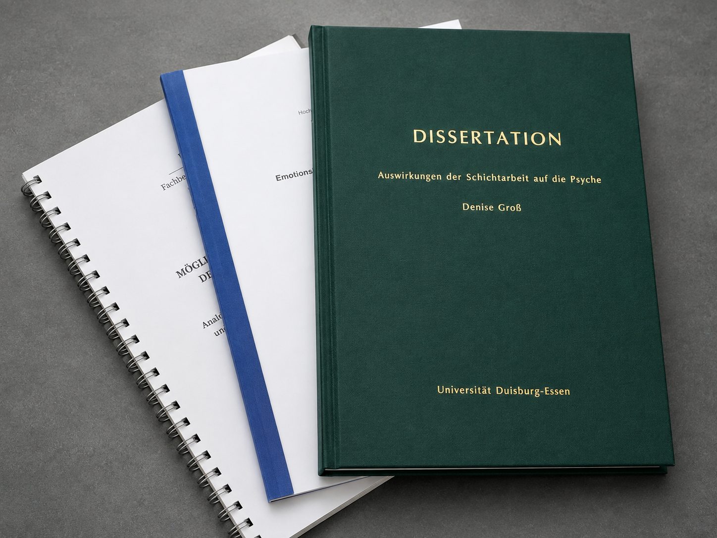 Dissertation im grünen Hardcover mit Goldprägung neben Softcover- und Spiralbindungen
